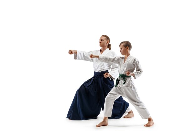 Man and teen boy fighting at Aikido training in martial arts school. Healthy lifestyle and sports concept. Fightrers in white kimono on white wall. Karate men with concentrated faces in uniform.