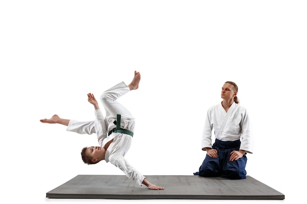 Man and teen boy fighting at Aikido training in martial arts school. Healthy lifestyle and sports concept. Fightrers in white kimono on white wall. Karate men with concentrated faces in uniform.