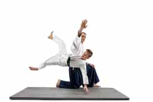 Free photo man and teen boy fighting at aikido training in martial arts school. healthy lifestyle and sports concept. fightrers in white kimono on white wall. karate men with concentrated faces in uniform.