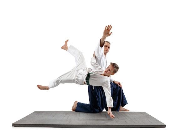 Man and teen boy fighting at Aikido training in martial arts school. Healthy lifestyle and sports concept. Fightrers in white kimono on white wall. Karate men with concentrated faces in uniform.