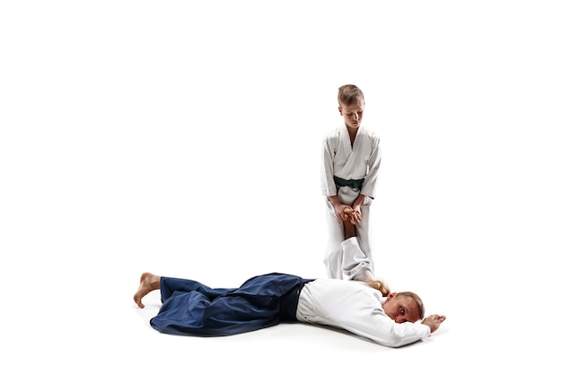 Man and teen boy fighting at Aikido training in martial arts school. Healthy lifestyle and sports concept. Fightrers in white kimono on white wall. Karate men with concentrated faces in uniform.