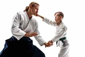 Foto gratuita uomo e ragazzo adolescente che combattono all'allenamento di aikido nella scuola di arti marziali. stile di vita sano e concetto di sport. combattenti in kimono bianco sul muro bianco