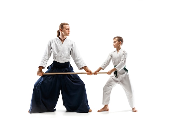 Мужчина и мальчик-подросток борются с деревянным мечом на тренировках по айкидо в школе боевых искусств. Концепция здорового образа жизни и спорта. Бойцы в белых кимоно на белом фоне. Мужчины каратэ в форме.