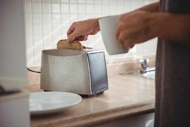 Man toasting bread for breakfast and drinking coffee