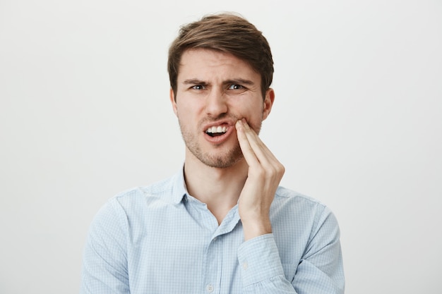 Мужчина трогает щеку и морщится от боли от зубной боли, нужен дантист