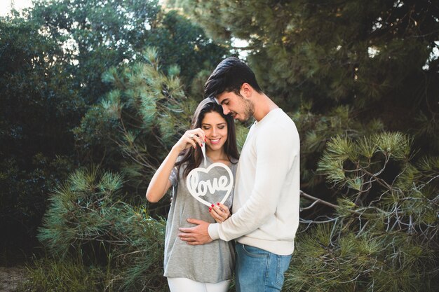 Man touching his girlfriend's belly and she holds a heart with the word "love" inside