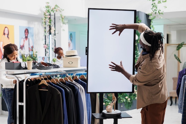 Foto gratuita uomo che tocca la lavagna interattiva per visualizzare la pubblicità di scarpe nel negozio di abbigliamento. cliente afroamericano che interagisce con lo schermo digitale bianco bianco mentre fa shopping nel centro commerciale