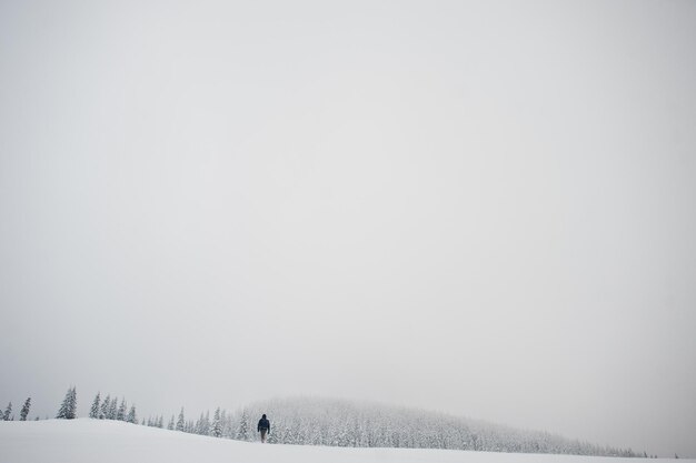 Man tourist photographer with backpack at mountain with pine trees covered by snow Beautiful winter landscapes Frost nature