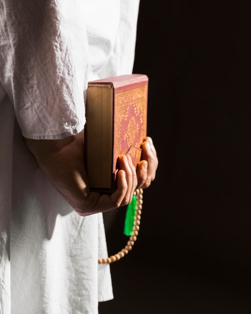 Free photo man in traditional arabic clothes holding quran behind his back