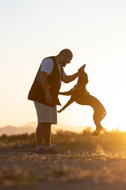 Мужчина тренирует свою собаку на открытом воздухе на закате