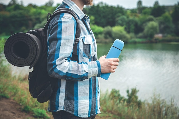 Free photo a man traveler with a backpack and a karemat holds a thermos in his hand