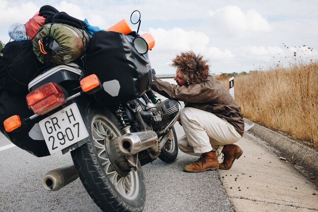 Человек пытается починить мотоцикл на обочине дороги