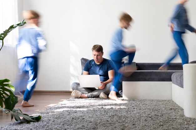 Man trying to work on laptop from home while her children are running around