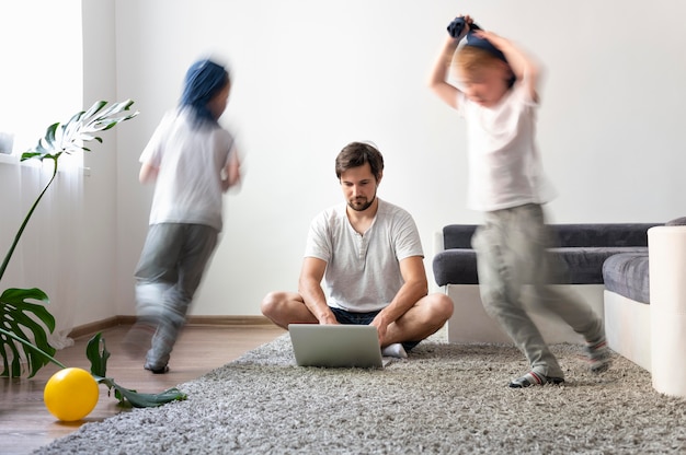 Uomo che cerca di lavorare su un laptop da casa mentre i suoi figli corrono in giro