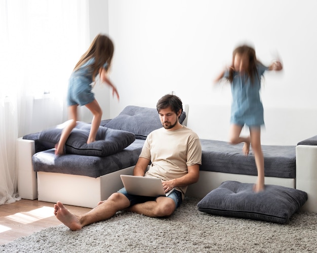 Free photo man trying to work on laptop from home while her children are running around