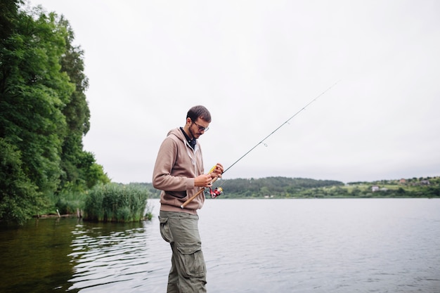 Man tying fishing lure on rod near the lake