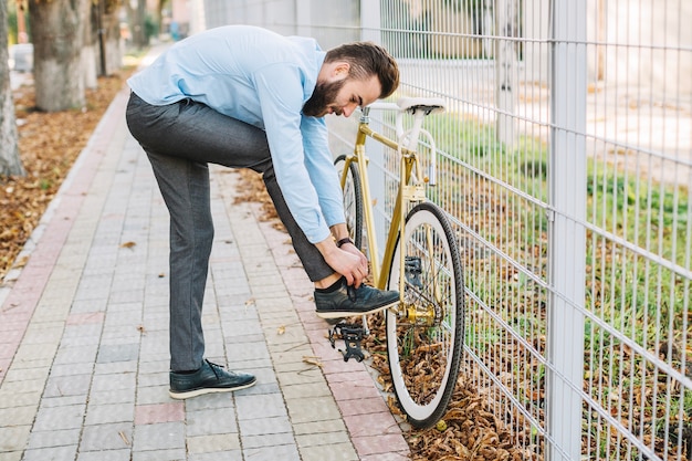 Foto gratuita uomo che lega i pizzi vicino alla bicicletta