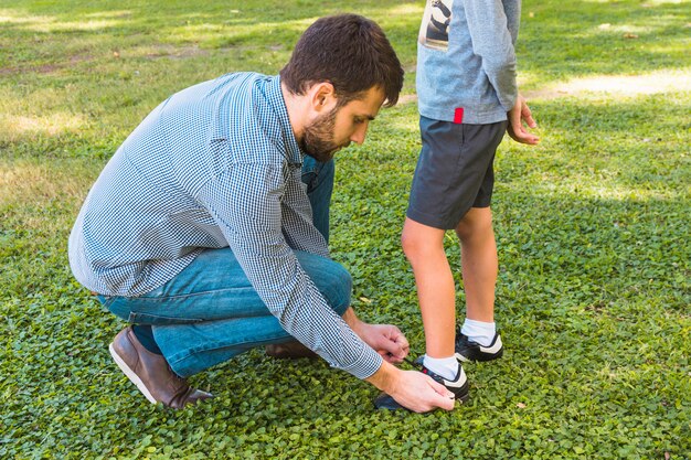 A man tying the shoelace of his son in the park