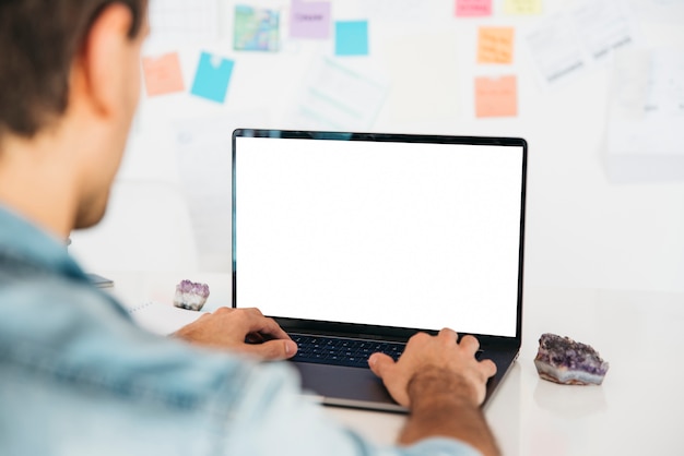 Man typing on laptop at desk near wall with notes