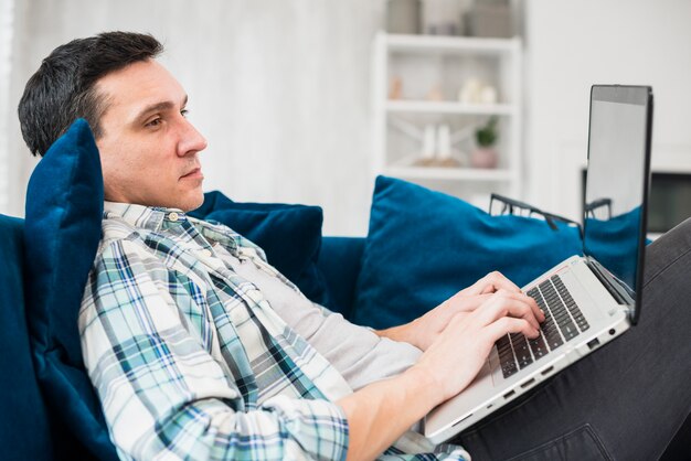 Человек печатает на ноутбуке и сидит на диване