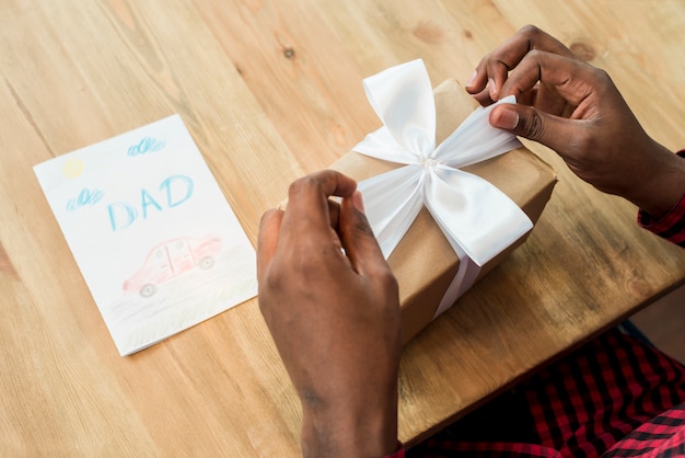 Man untying bow on gift box near greeting card