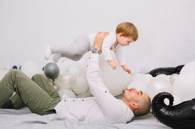 Мужчина поднимает маленького ребенка на руки и лежит на кровати