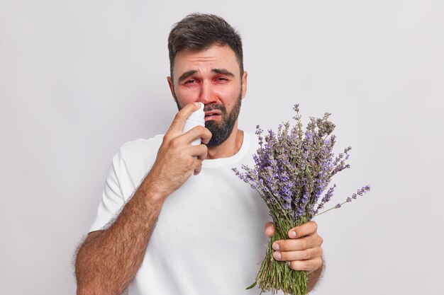 남자는 코막힘에 에어로졸 스프레이를 사용하여 라벤더 꽃다발을 들고 알레르기 질환 증상이 흰색으로 격리된 캐주얼 티셔츠를 입는다