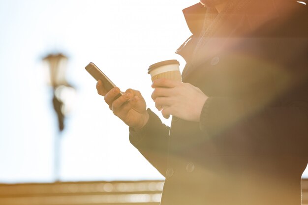 Человек с помощью мобильного телефона и пить кофе на улице в солнечный день