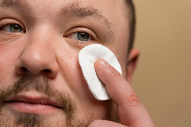 Man using cotton pad on his face for skincare