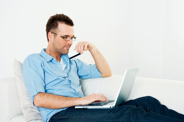 Man using credit card and laptop on couch