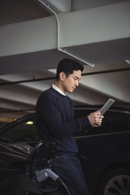 電気自動車の充電中にデジタルタブレットを使用している男