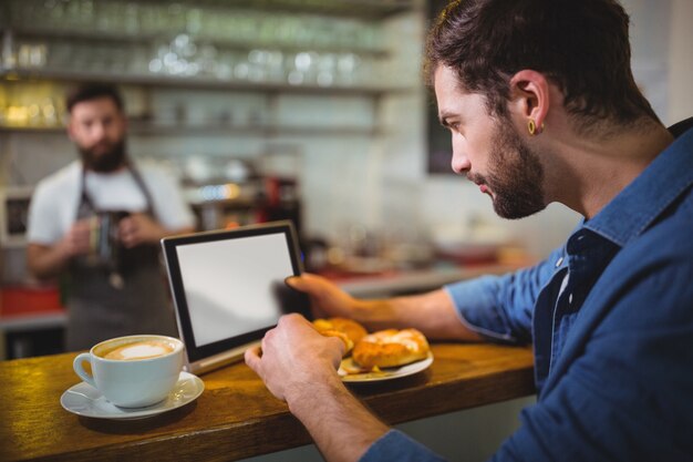 Man using digital tablet while having croissant in cafÃ©