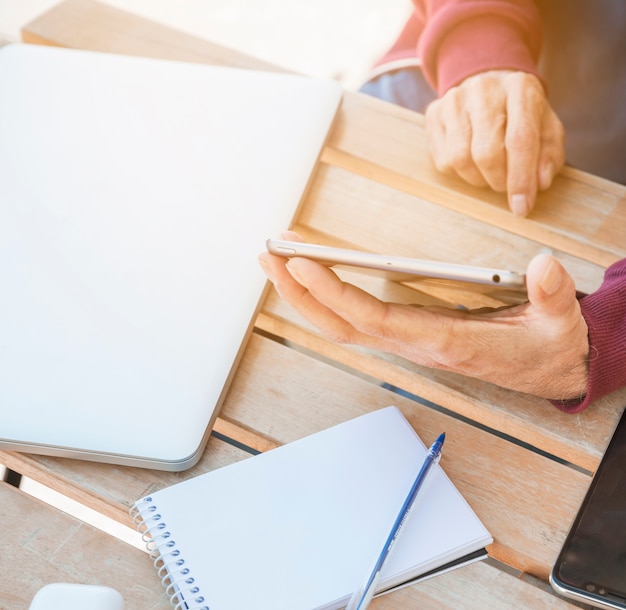 Man using digital tablet with laptop; spiral notepad and pen on wooden desk