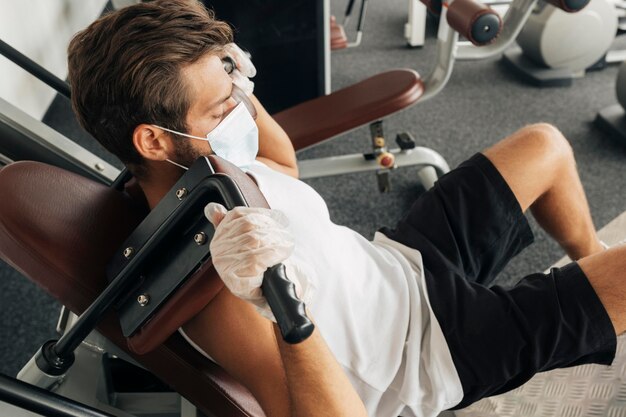 Человек, использующий оборудование в тренажерном зале, в медицинской маске