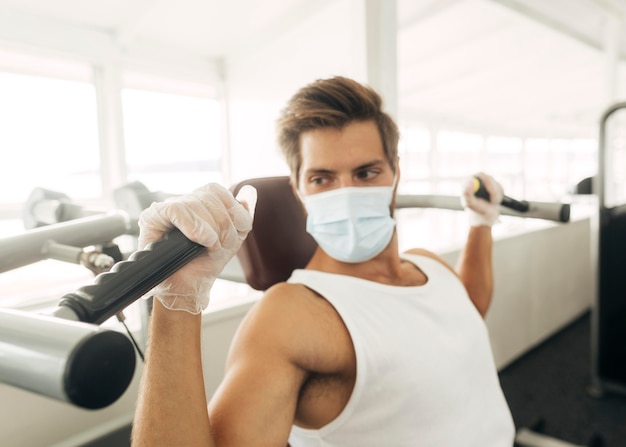 Foto gratuita uomo che utilizza attrezzature da palestra mentre indossa la maschera medica