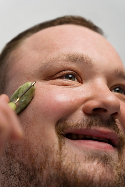 Free photo man using jade roller on his face for skincare