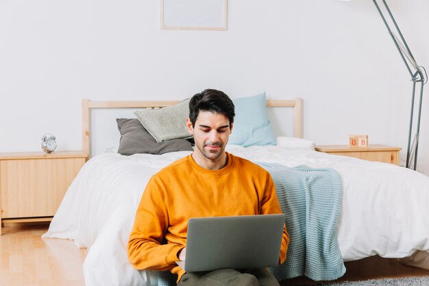 Uomo che utilizza computer portatile vicino al letto comodo