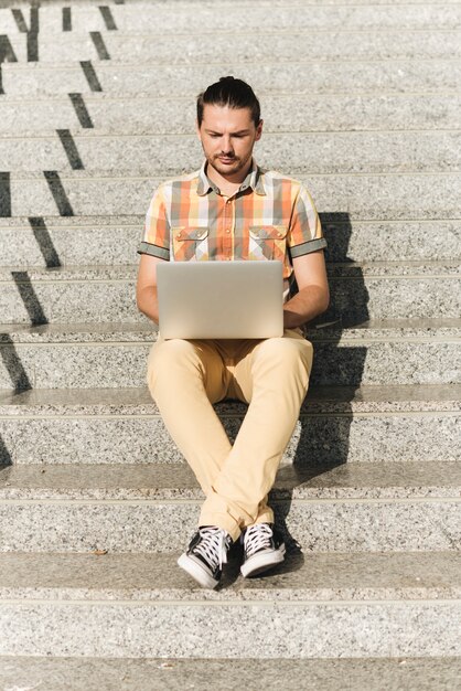 Free photo man using laptop on stairs