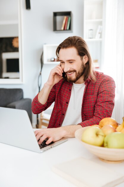 ラップトップを使用して、自宅で携帯電話で話している人