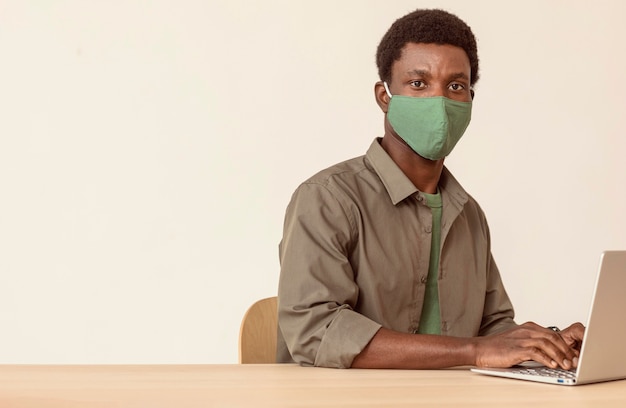Человек, использующий ноутбук и в зеленой медицинской маске