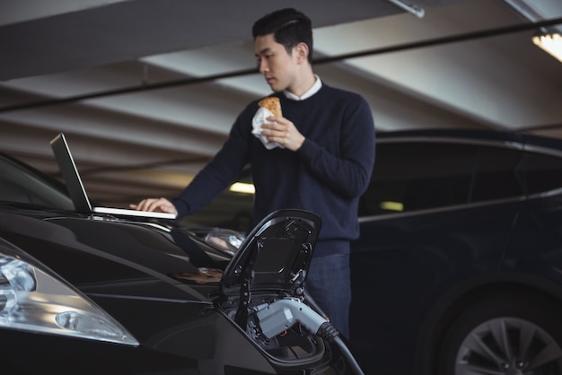 Man using laptop while charging electric car