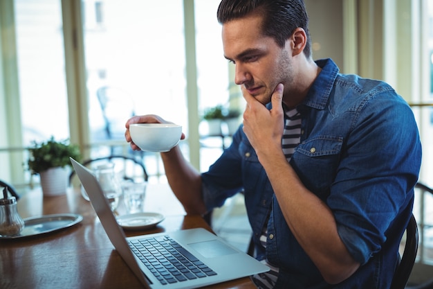 コーヒーを持ちながら男のラップトップを使用して、