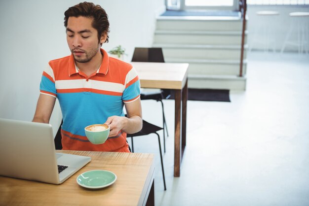 コーヒーを飲みながらノートパソコンを使用している人