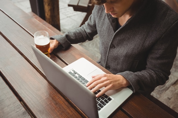 Uomo che per mezzo del computer portatile mentre mangiando bicchiere di birra