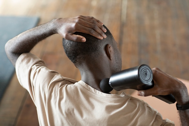 man using massage gun on neck high angle