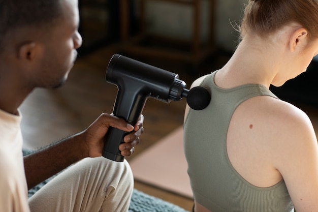 Free photo man using massage gun on woman high angle