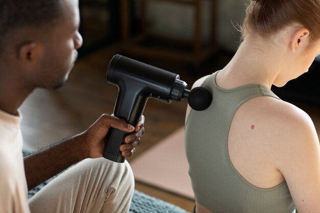 man using massage gun on woman high angle