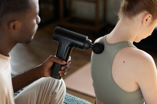 Man using massage gun on woman high angle