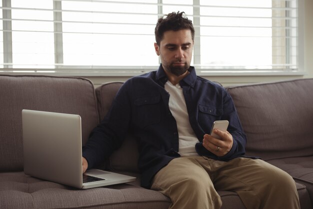 Man using mobile phone and laptop on sofa