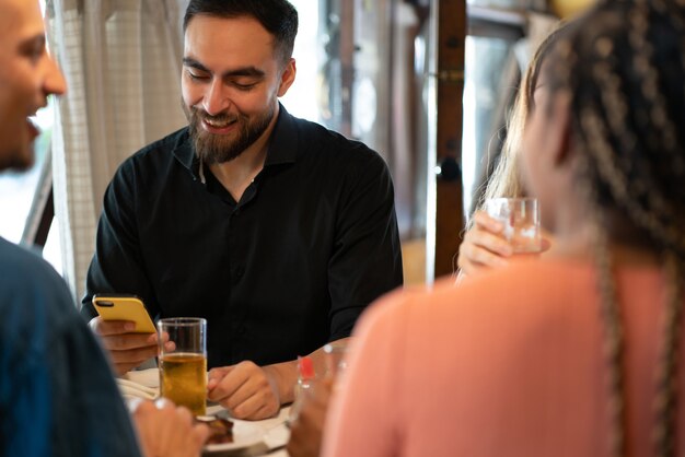 Человек, использующий мобильный телефон, выпивая стакан пива со своими друзьями в баре.